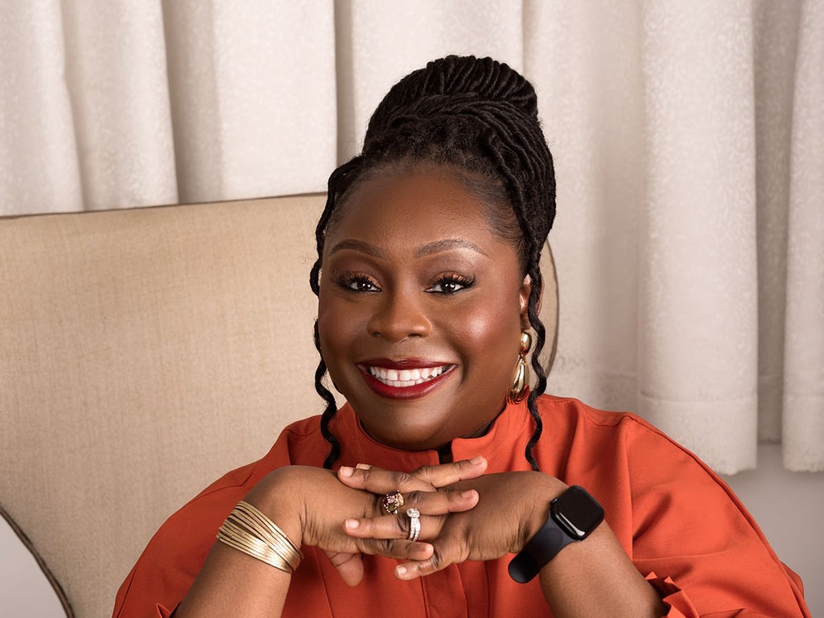 Dr Itunu Johnson smiling, wearing an orange blouse, with her hands folded beneath her chin.